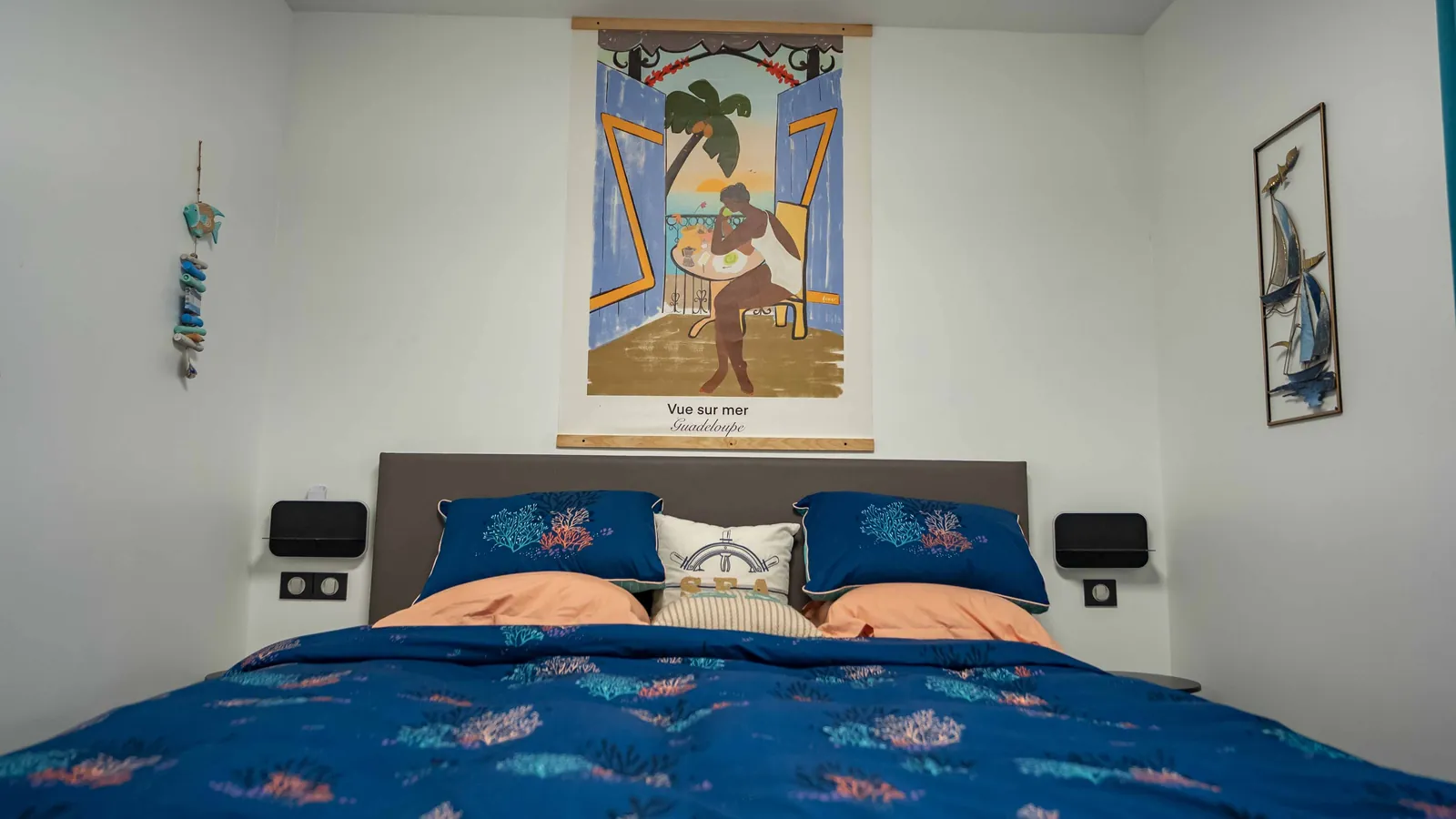 Chambre Sea World — lit bleu corail et affiche « Vue sur mer, Guadeloupe », villa House of Harmony, Goyave